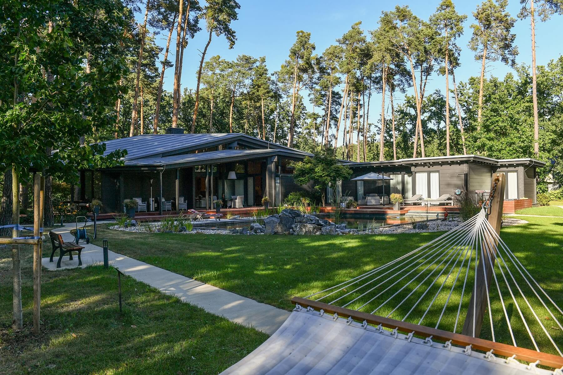 Residence RR mezi vzrostlými borovicemi, koupací jezírko a trávník před hlavní terasou